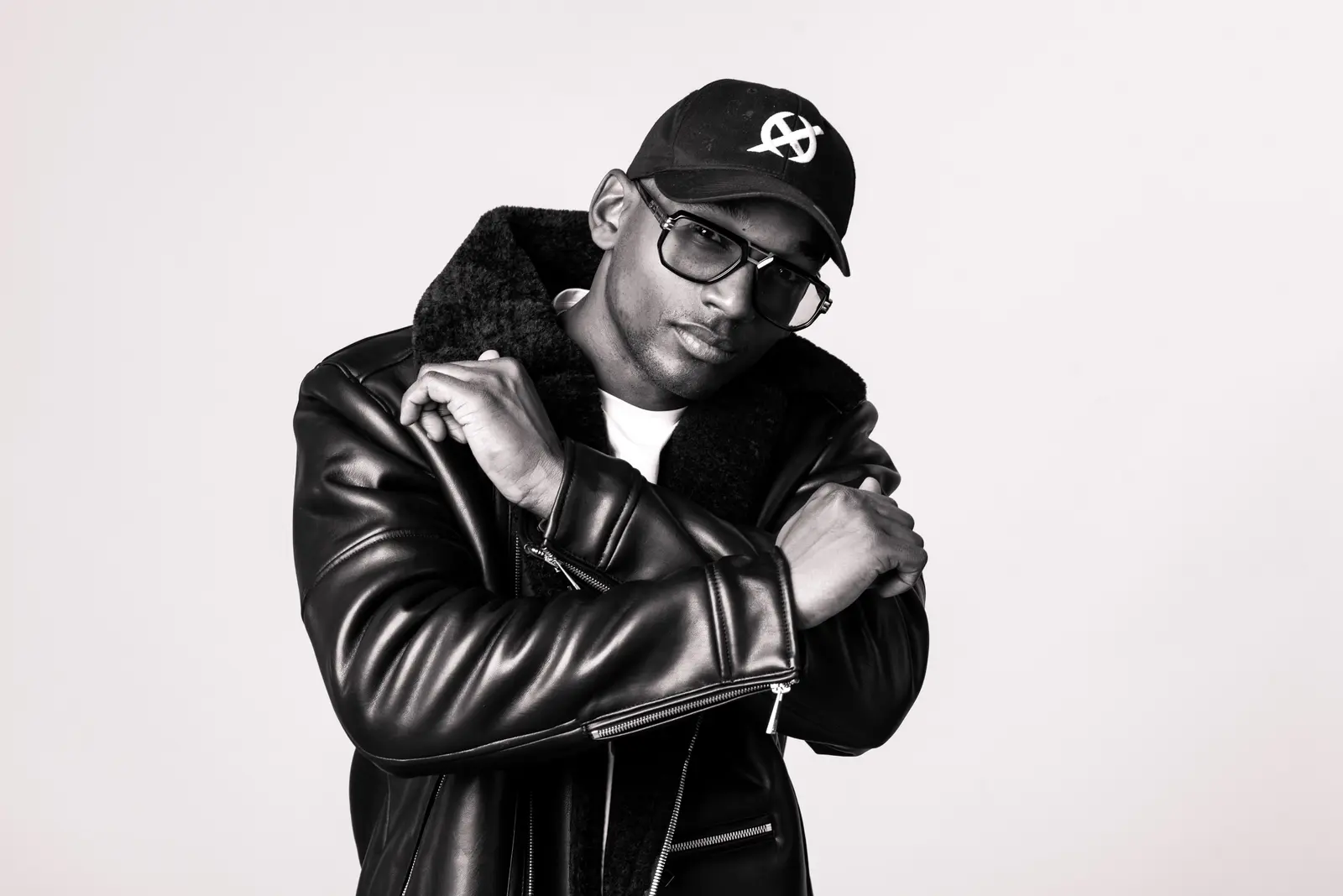 Hurrican X in a black cap and leather jacket, arms crossed, studio portrait